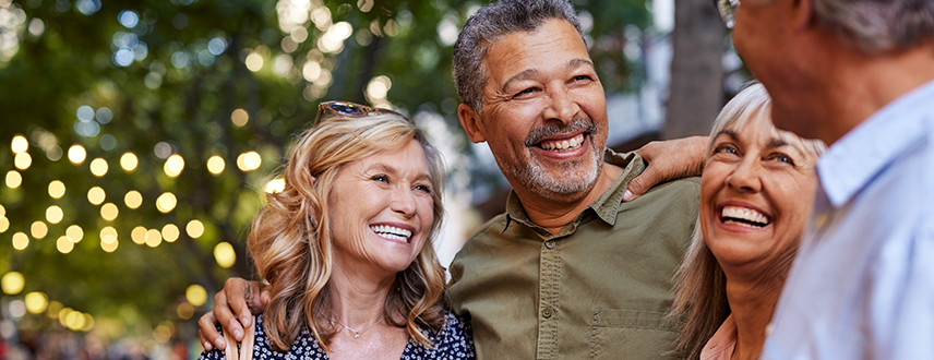Three friends in their 50s and 60s laughing together outdoors, representing healthy aging and staying socially connected.
